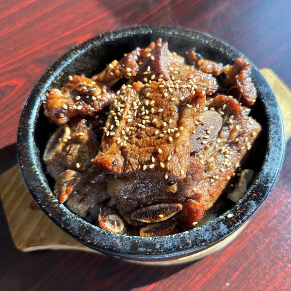 Kimchi House's Korean BBQ short ribs (galbi) with sesame seeds, served in a black stone bowl.