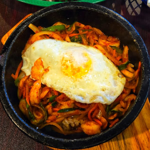 Korean bibimbap with a fried egg, vegetables, and rice in a black stone bowl.