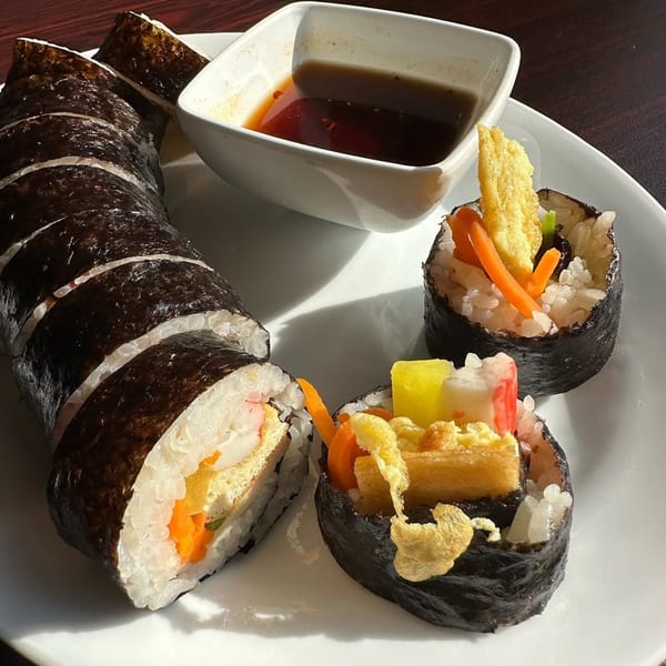 Platter of sliced Korean gimbap rolls with various fillings and a side of dipping sauce.